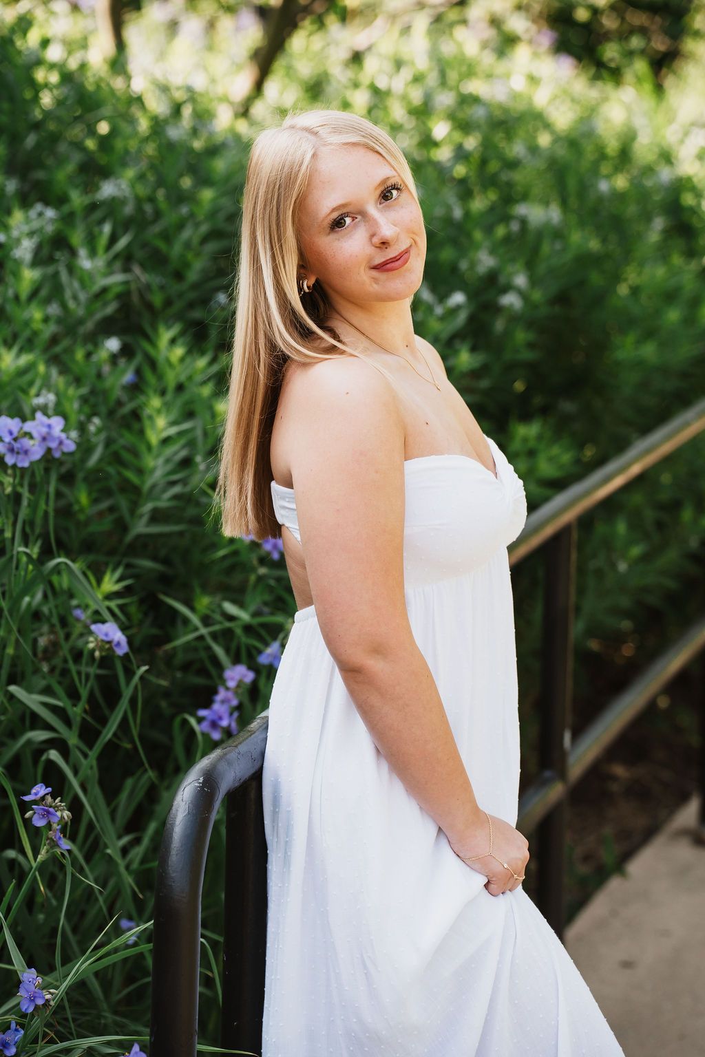White dress photoshoot along a garden path with blooming purple iris flowers.