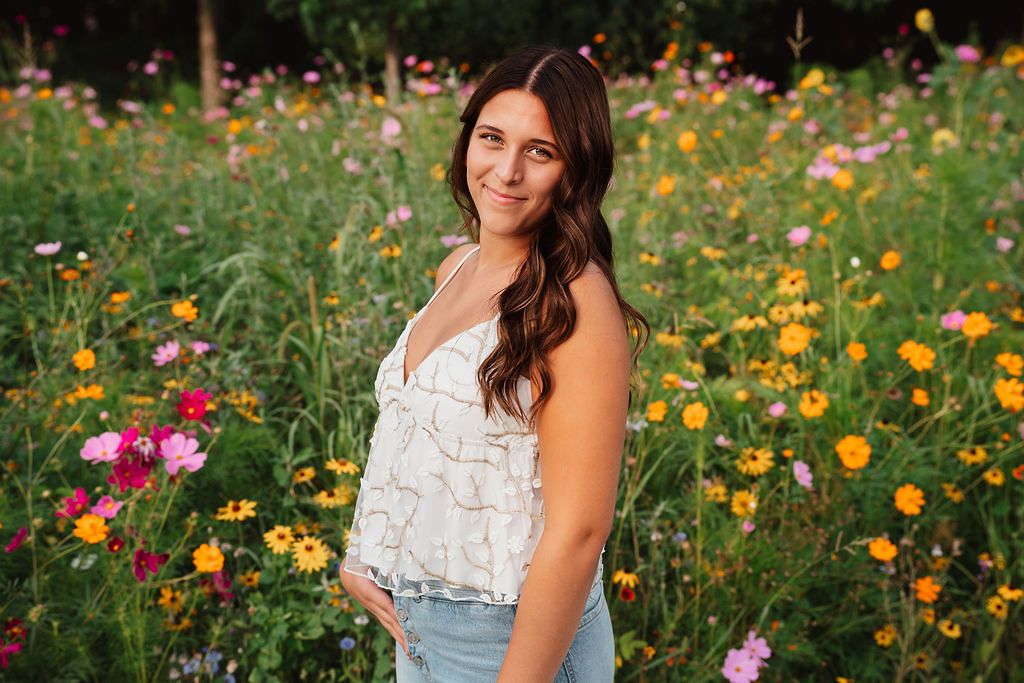 Young woman in white lace top posing in a vibrant wildflower field with pink and yellow blooms.
