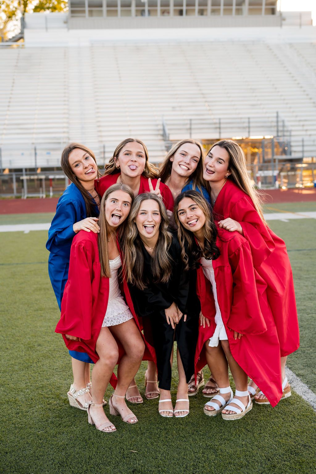 A group wearing red graduation gowns poses together crouching on a football field.
