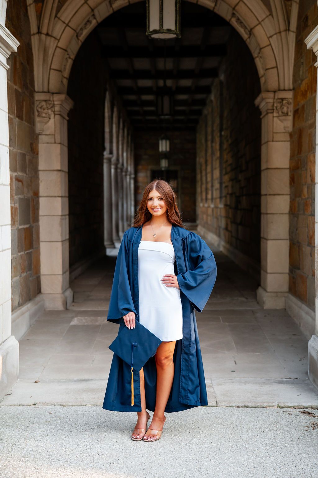 A person wearing a blue graduation gown sits in an arched stone hallway in a series of three similar poses.