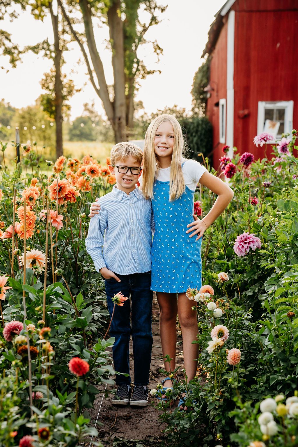 Children pose together in colorful dahlia garden next to red barn.