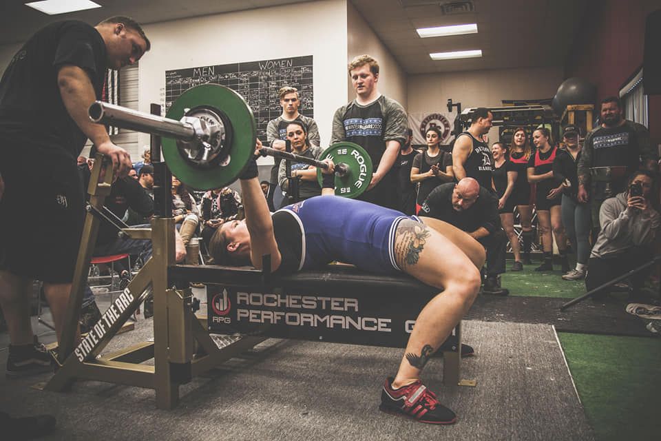 Athlete performing a heavy bench press at a Rochester Performance powerlifting competition.