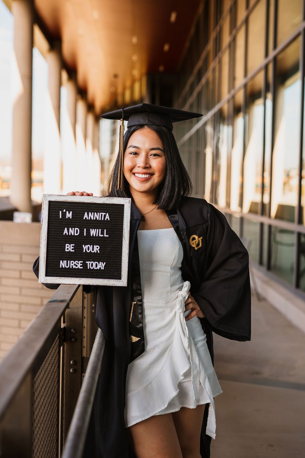 Nursing graduate holds letter board signs in a covered walkway for graduation photos.