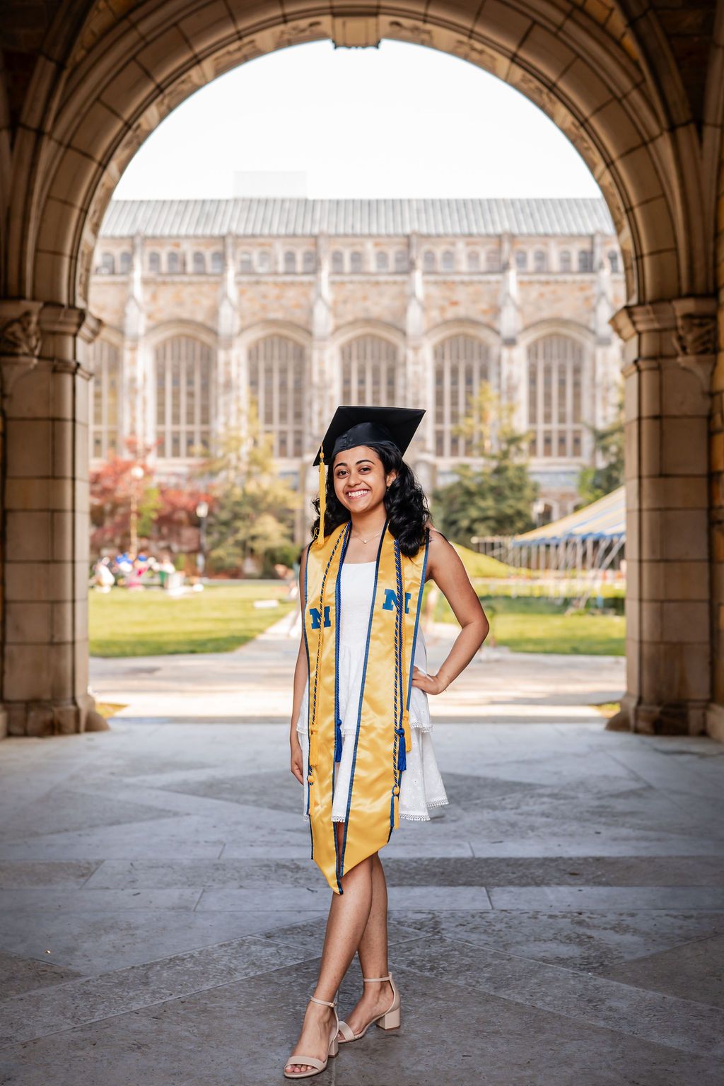 A graduate poses in cap and gown under stone archways on a university campus during graduation photo session.