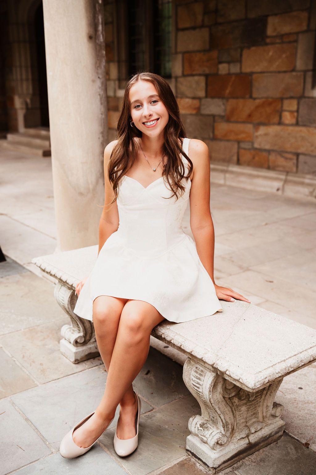 Woman in white dress sitting on stone bench in series of casual lifestyle portraits.