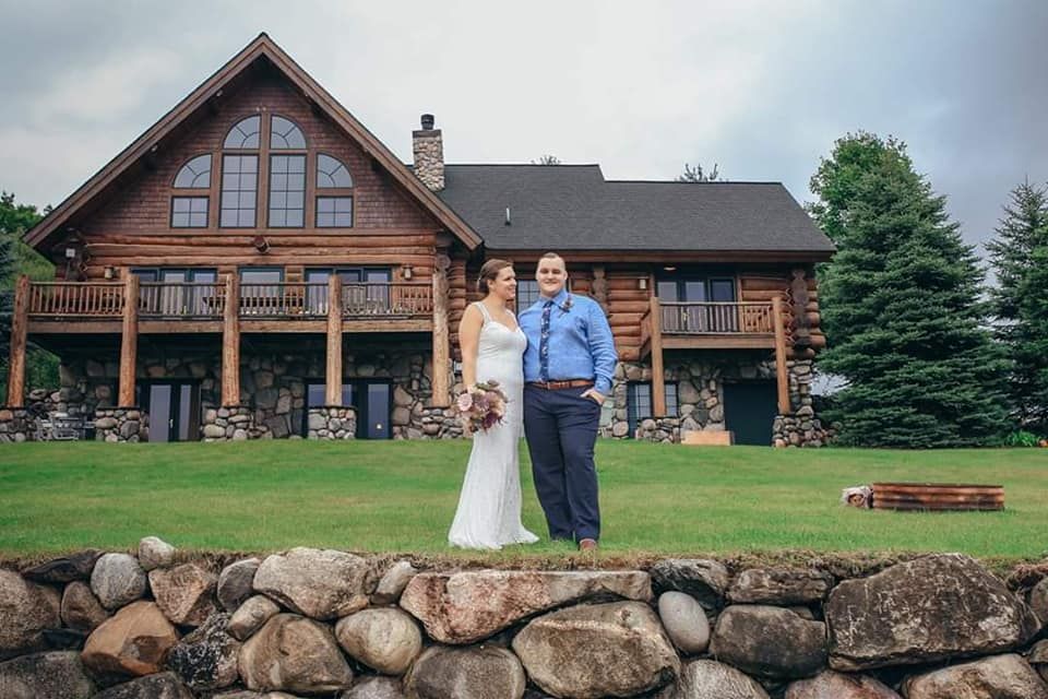 Bride and groom posing in front of a rustic log cabin venue on their wedding day.