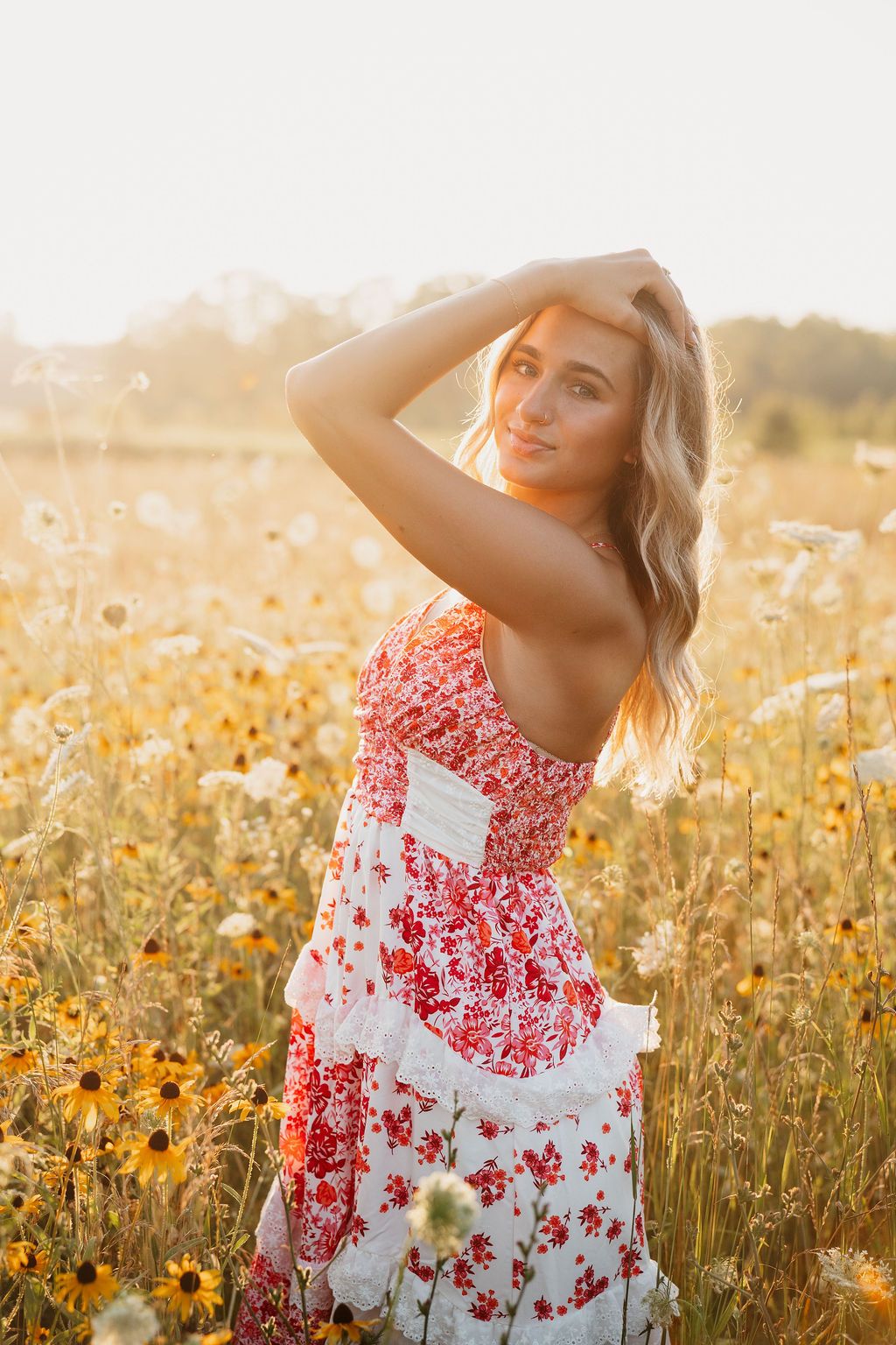Summer fashion portrait in a meadow with red and white floral dress against golden sunlight.