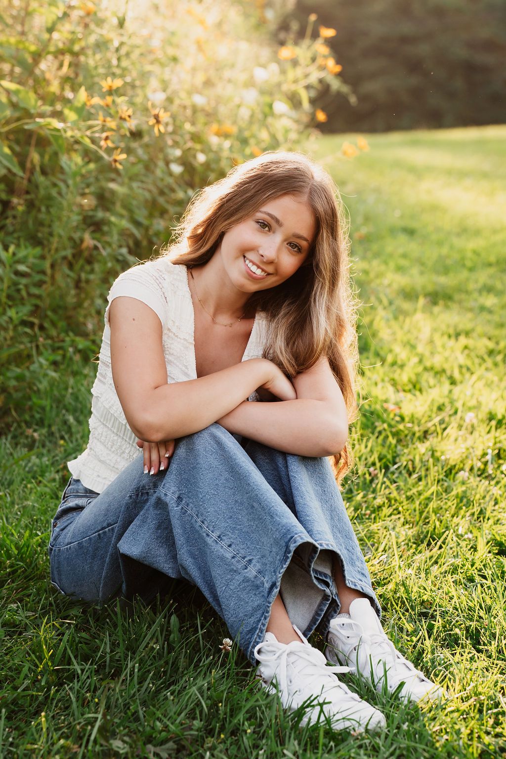A casual outdoor portrait sitting in grass wearing jeans and white sneakers during golden hour.