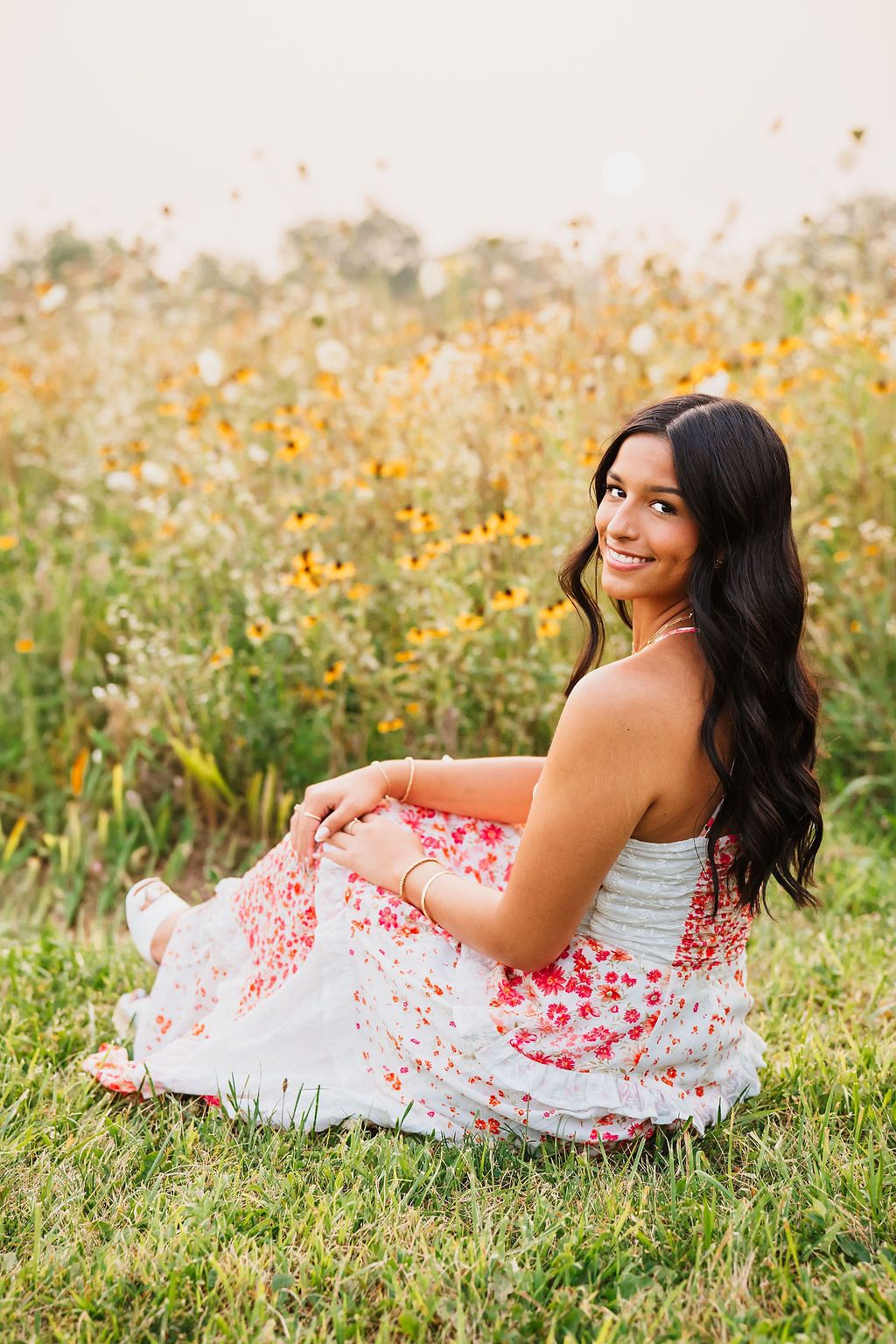 Senior portrait in floral dress laying in wildflower field during golden hour.