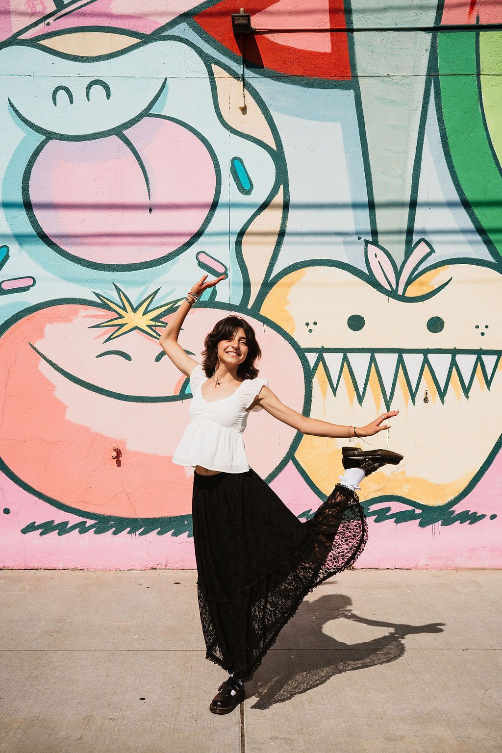 Person dancing in front of colorful street art mural wearing white top and black skirt. Eastern market senior photos, PCEP Senior Photos