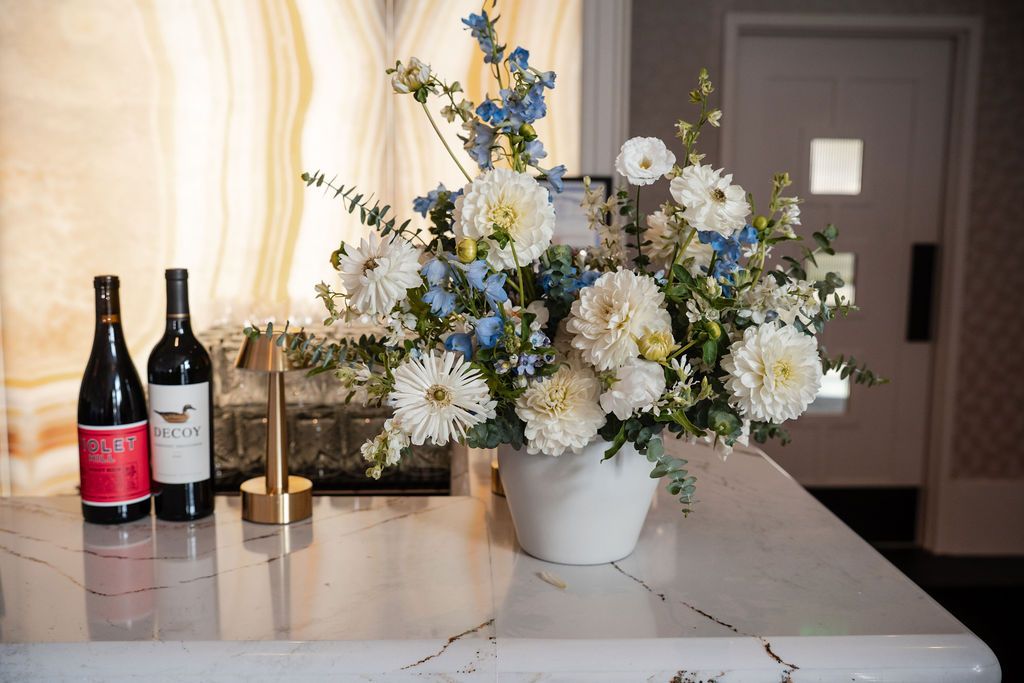 Wedding reception table decor with blue and white floral arrangements and wine bottles.