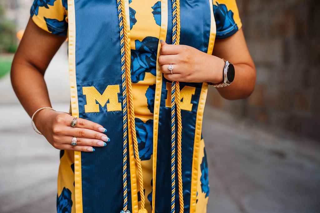 Graduate wearing blue and yellow University of Michigan graduation stole with gold honor cords for commencement ceremony.