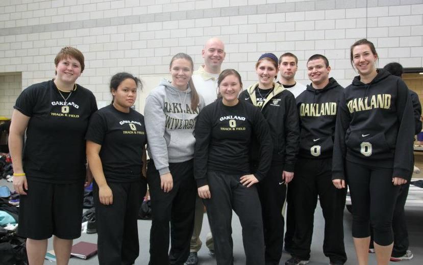 Group of nine people in Oakland athletic wear posing together indoors at a sports facility.