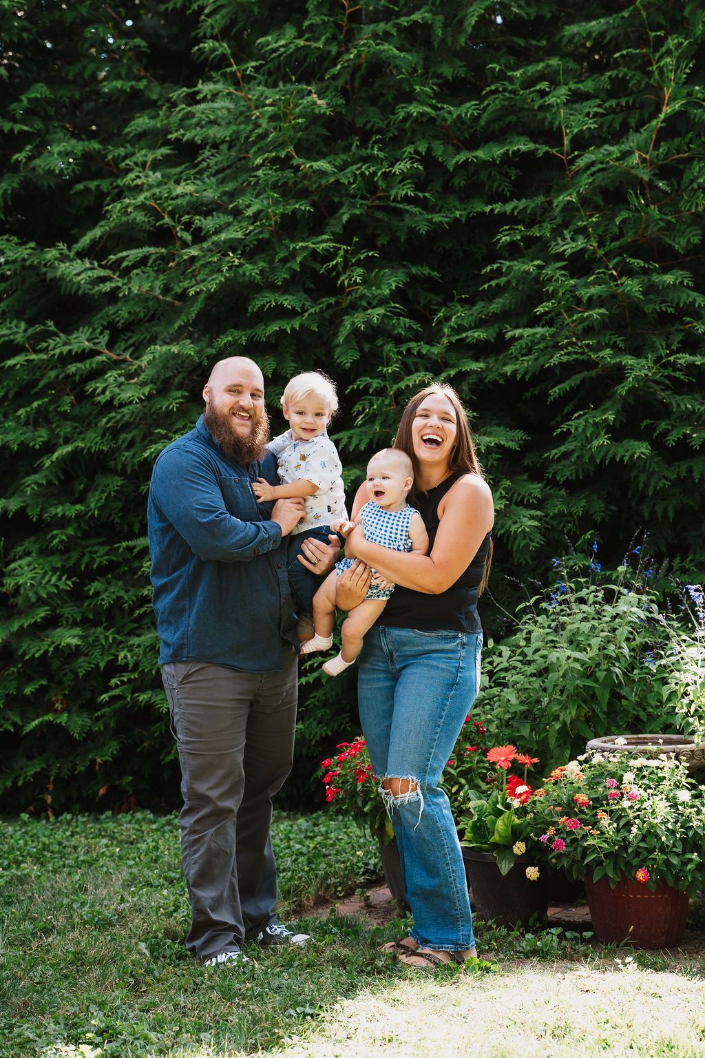 Joyful family interaction outdoors against a backdrop of green trees and red flowers.