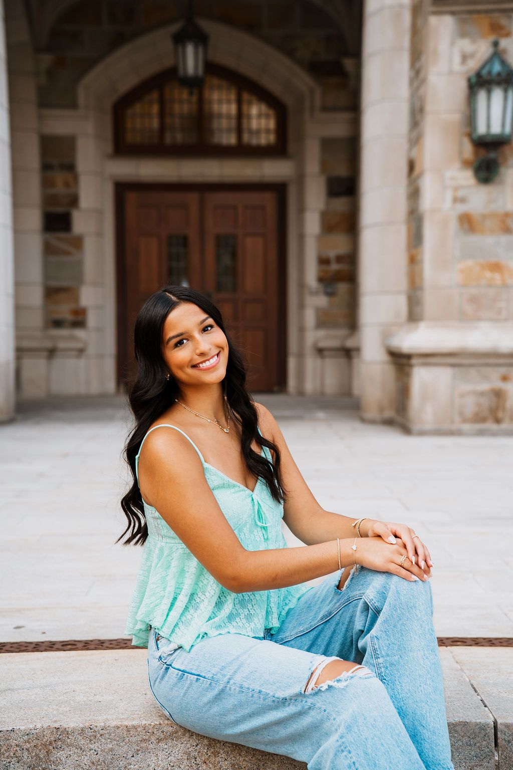 Casual portrait session against stone architecture wearing a mint colored top and light wash denim.