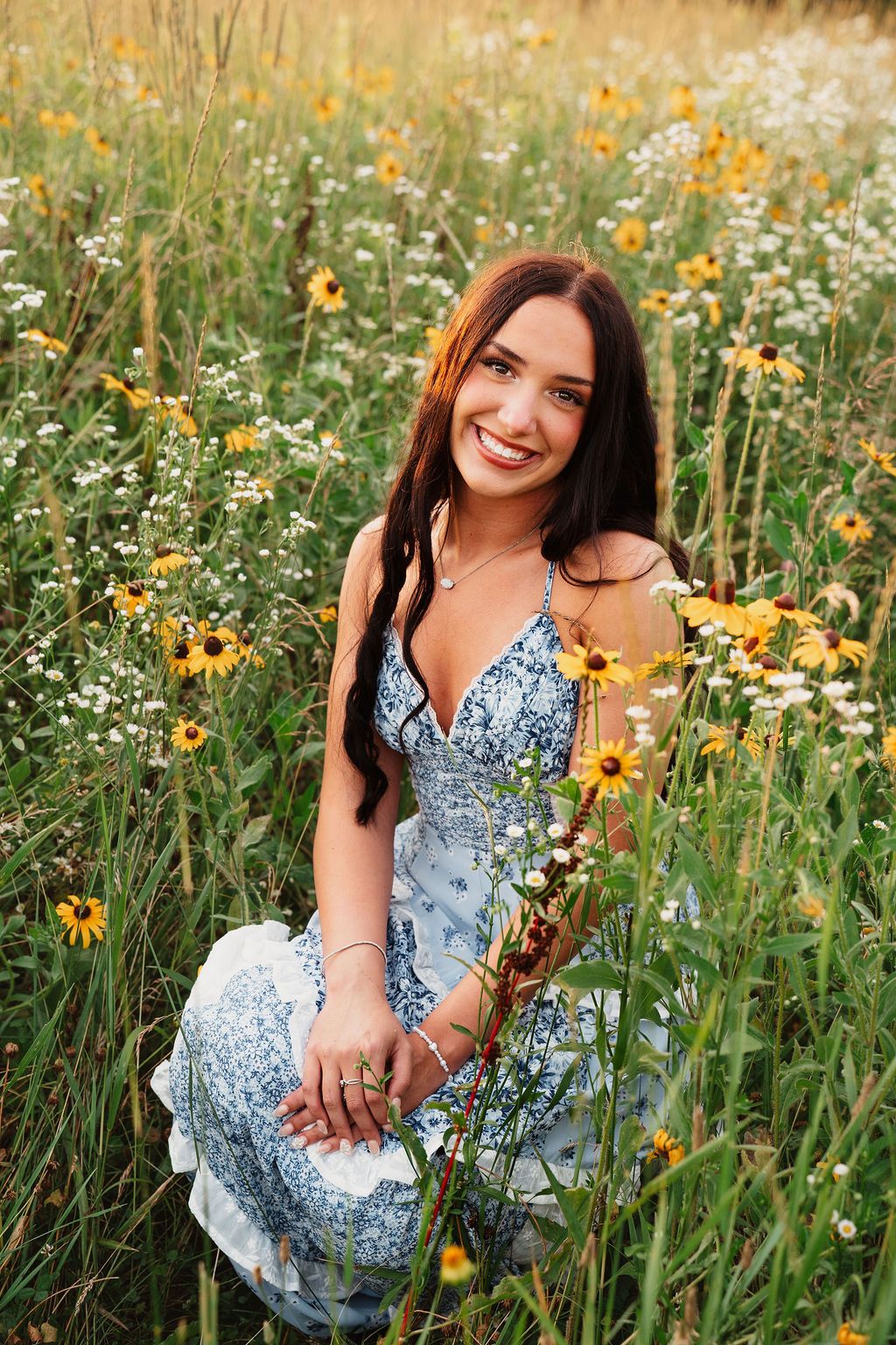 A person in a blue floral dress poses joyfully among yellow wildflowers and daisies in a summer meadow.