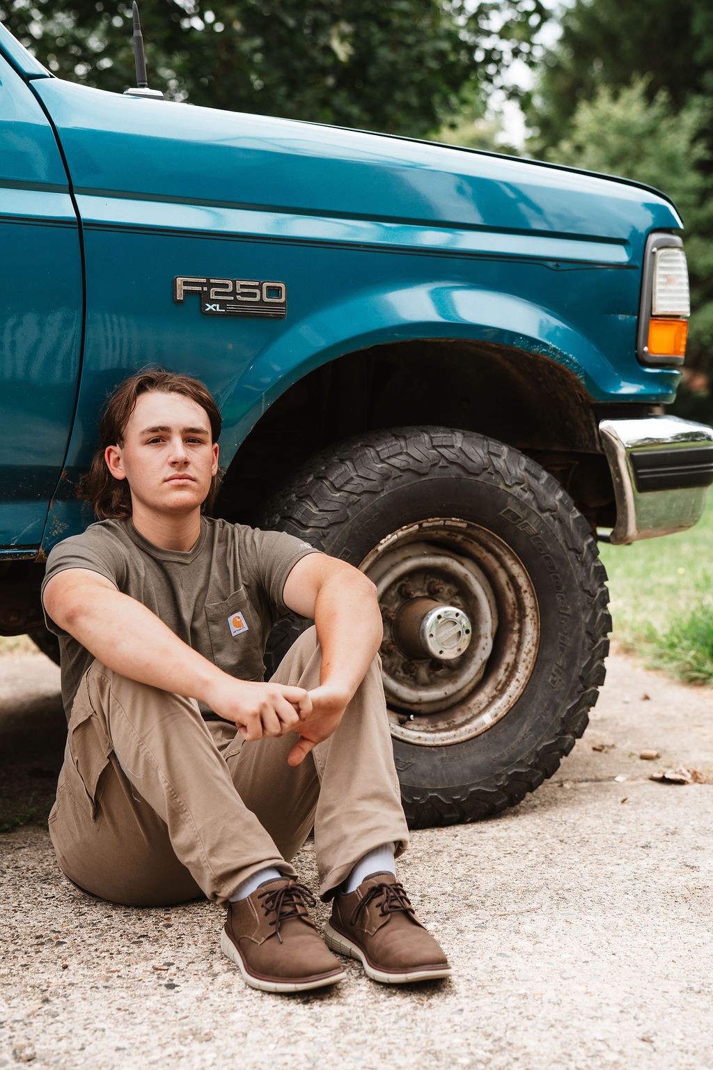 A sequence of casual poses sitting next to a blue Ford F250 truck on a gravel surface.