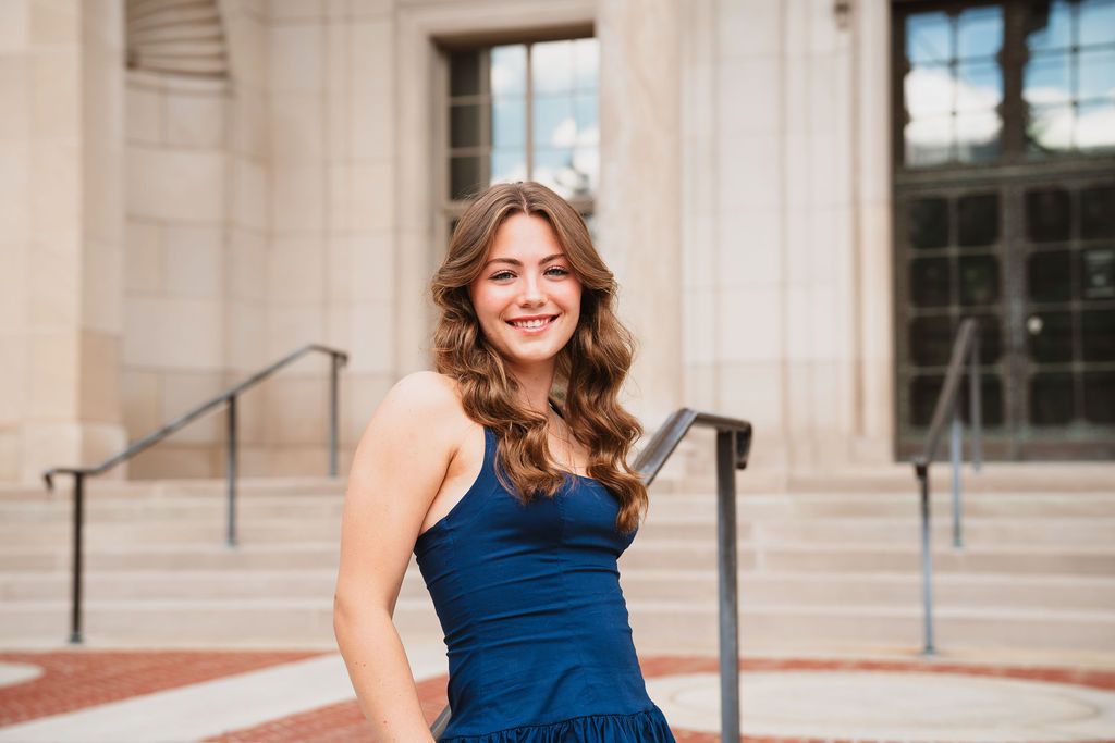 Woman in navy blue dress poses elegantly on outdoor stone steps.