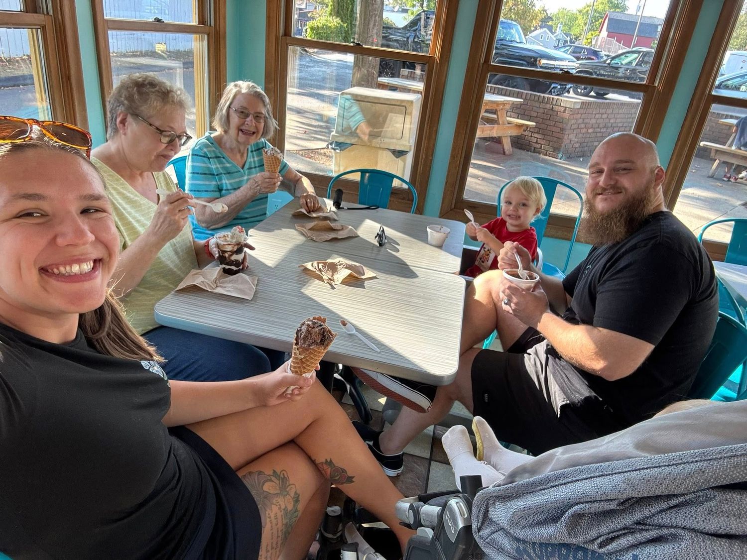 Family group smiles while enjoying ice cream together at a bright seaside restaurant with large windows.