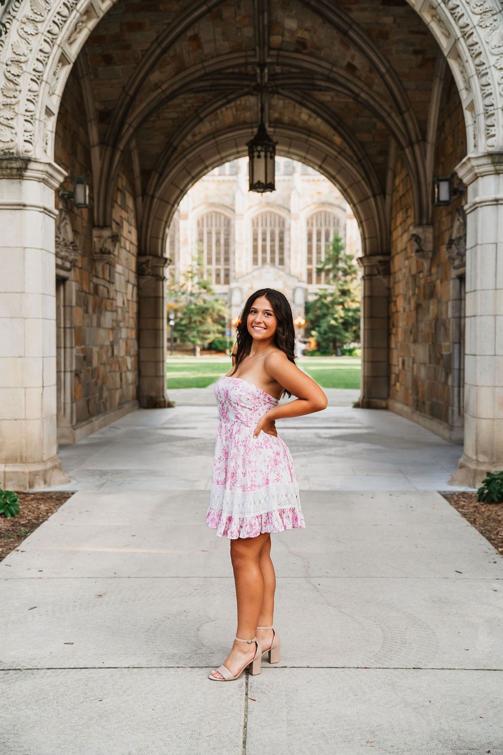 A pink floral dress is showcased in a series of photos under a grand stone archway corridor.