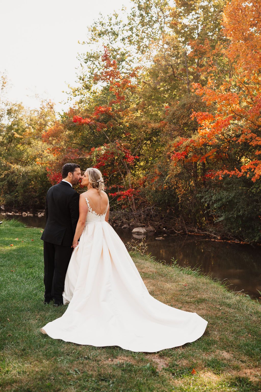 Newlyweds share intimate moment against backdrop of vibrant fall foliage and red flowers.
