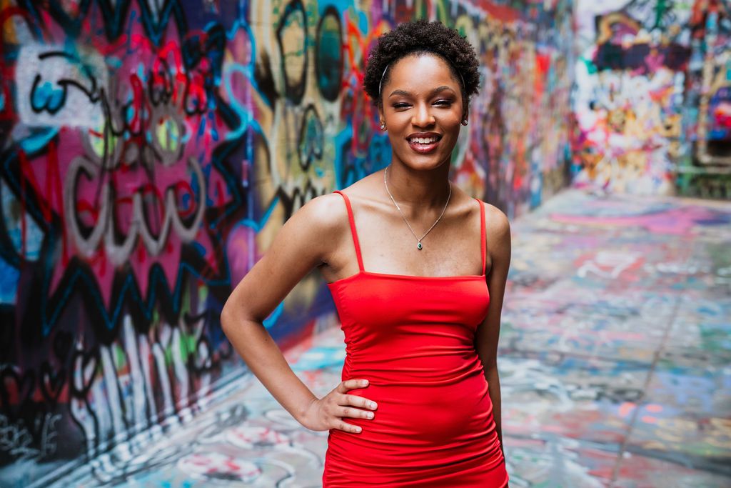 A person in a vibrant red dress poses confidently against a colorful graffiti wall backdrop.