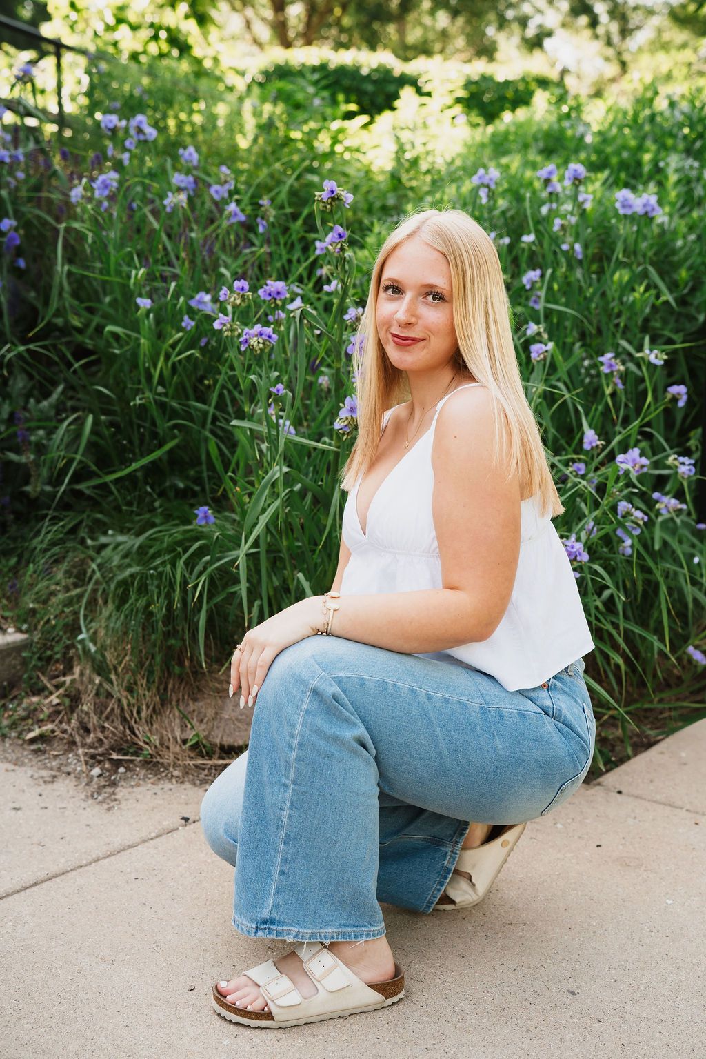 Person in casual attire sitting on concrete near purple flowers in a garden.