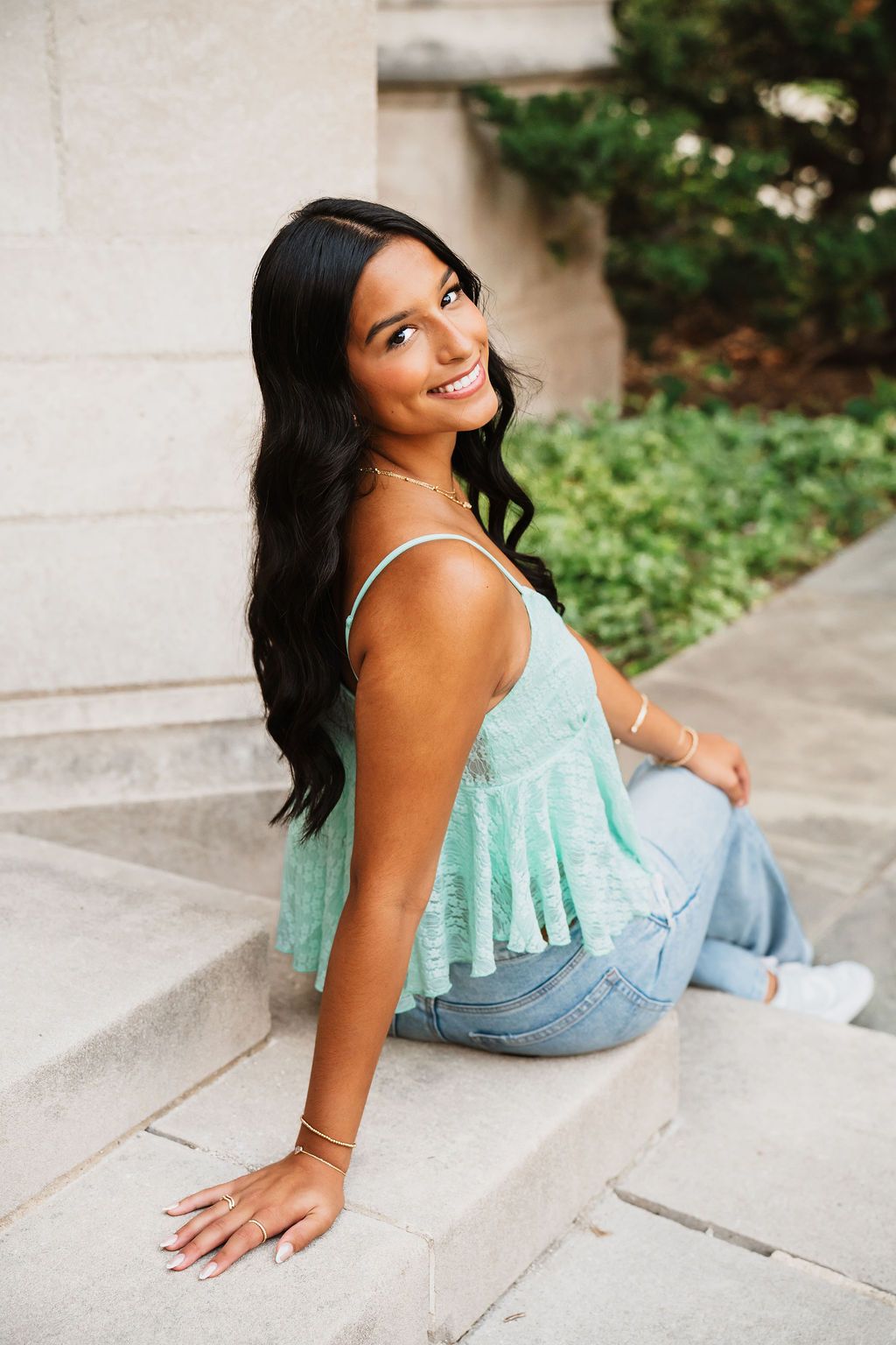 A person in a mint green top and jeans poses casually on stone steps outdoors.
