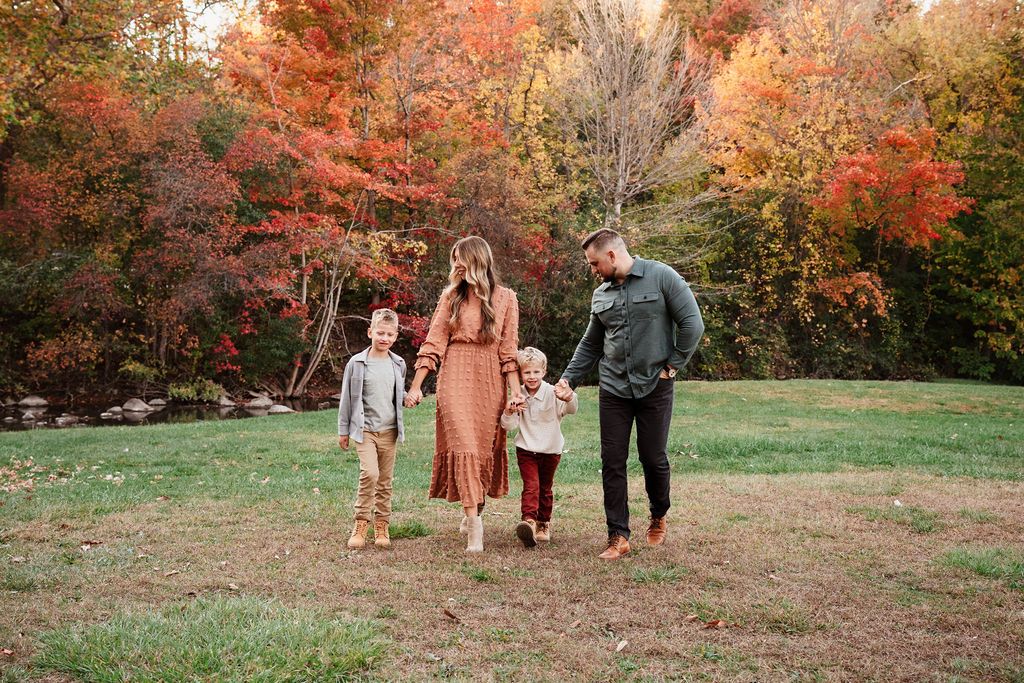 Family of four walking in a field surrounded by vibrant fall foliage during an autumn photo session.