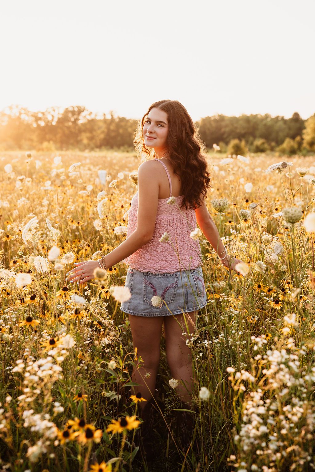 A person stands in a wildflower meadow at golden hour wearing a pink top and denim shorts.