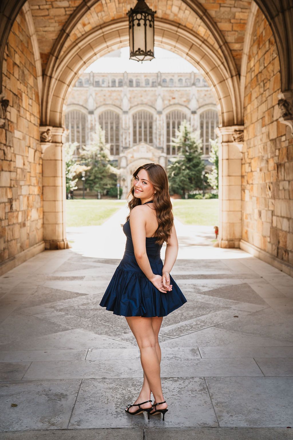 A portrait taken under an ornate stone archway with Gothic university architecture visible in the background.