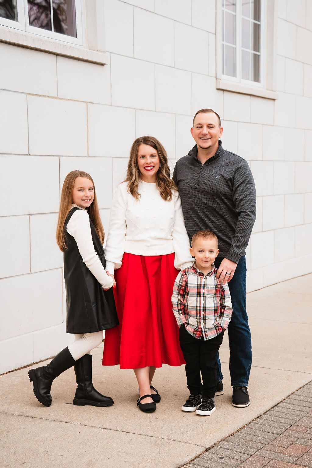 Classic family portraits against white stone wall featuring coordinated red and black attire.