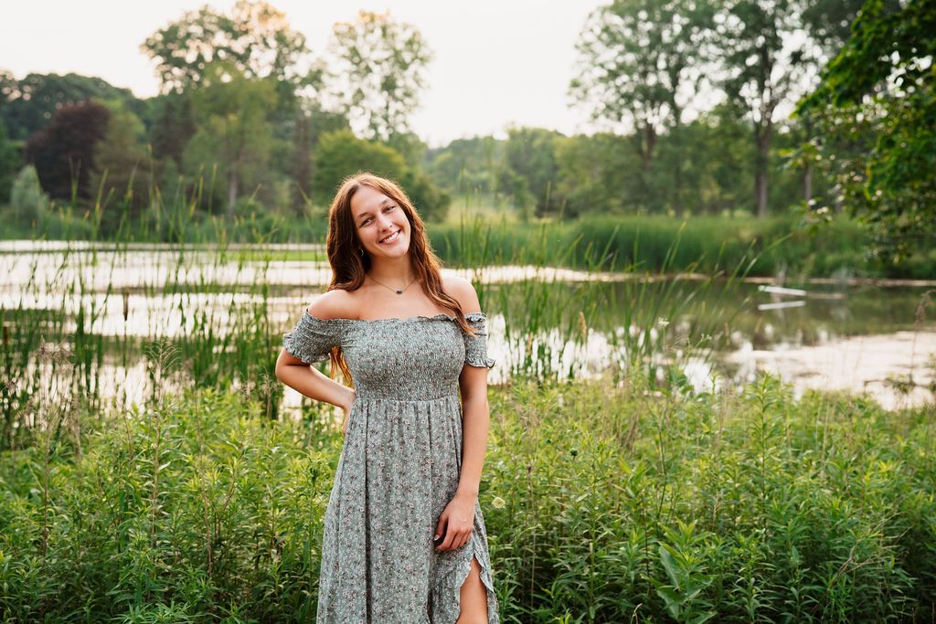 A floral off-shoulder dress sways in a summer meadow by a tranquil lake during golden hour.