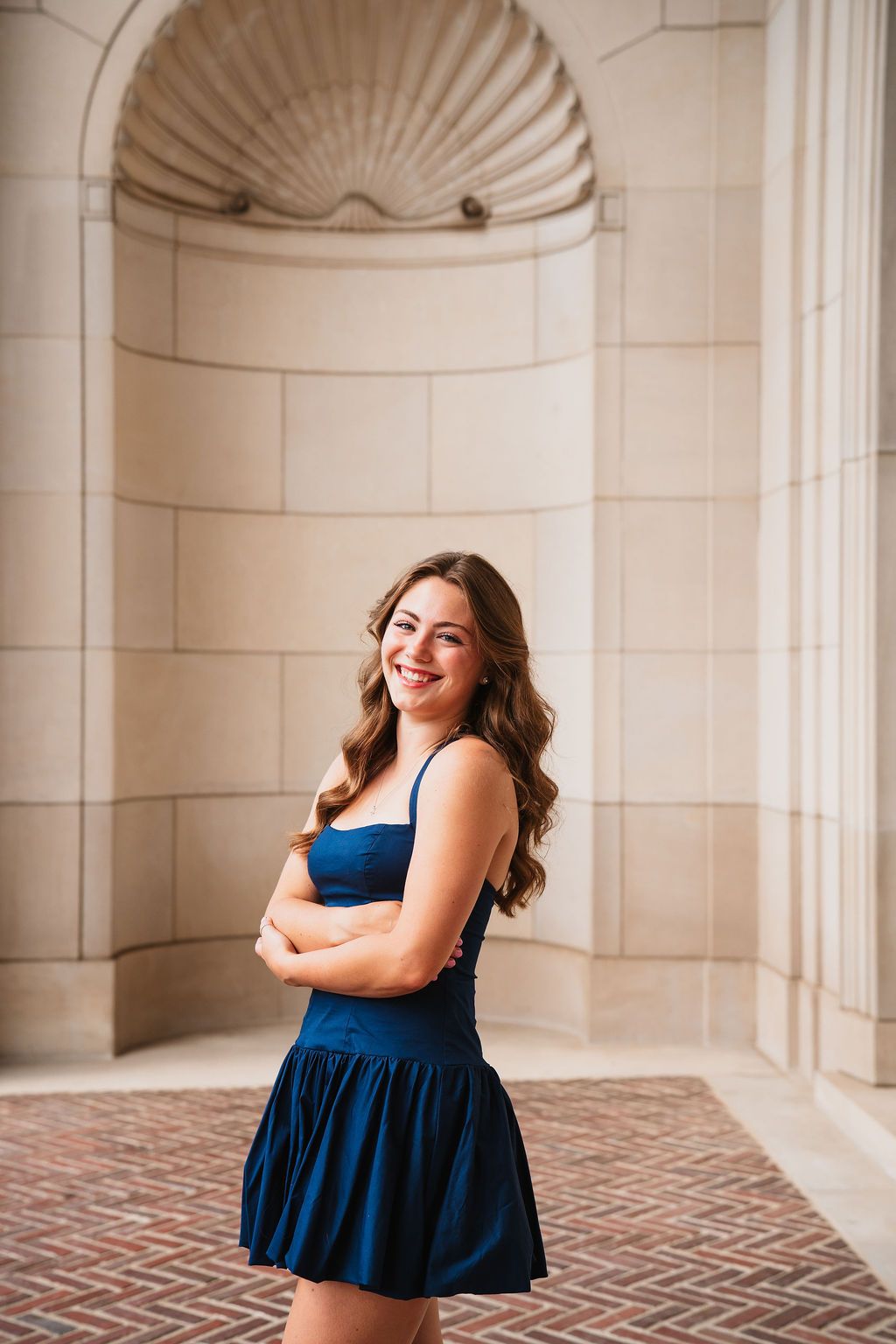 A person in a navy dress strikes various poses in front of an elegant architectural backdrop with arched details.