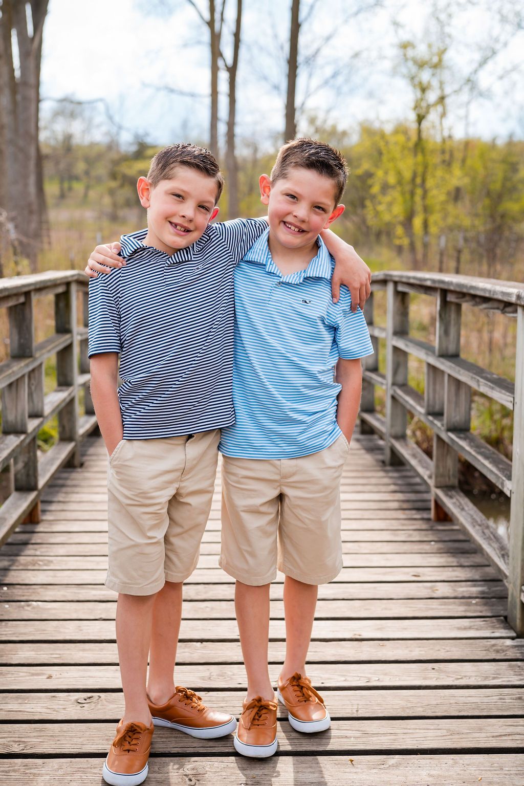 Two young boys in coordinating outfits pose together on a wooden boardwalk during a spring outdoor photoshoot.