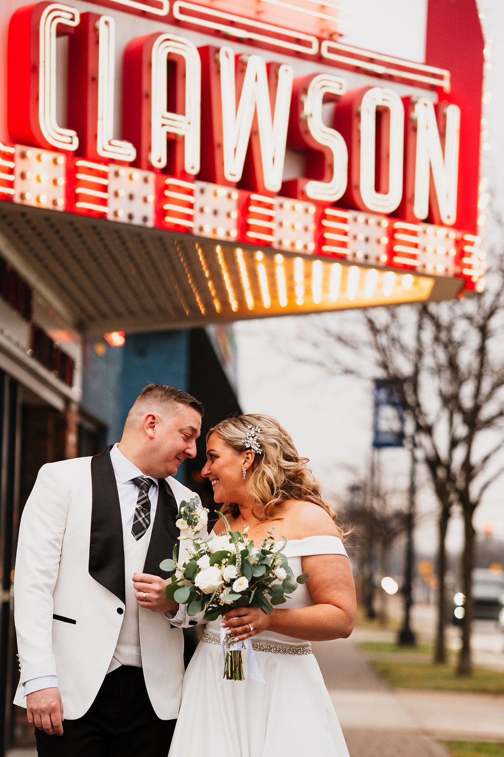 Wedding couple poses romantically under vintage theater marquee lights.