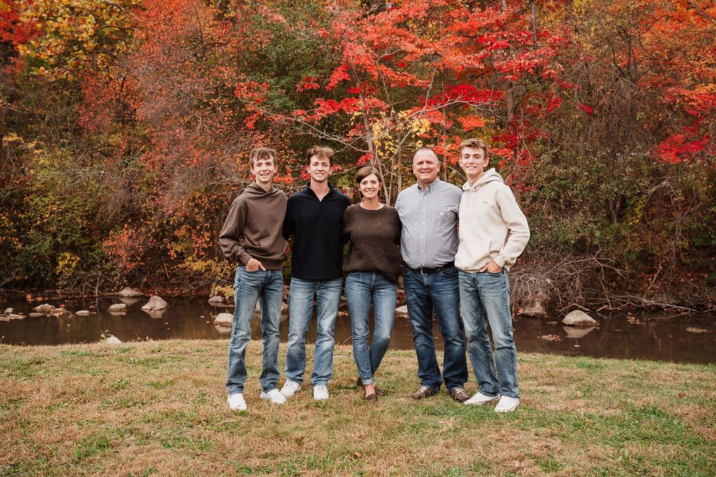 Family of five posing outdoors in fall foliage with vibrant red and orange trees in background.