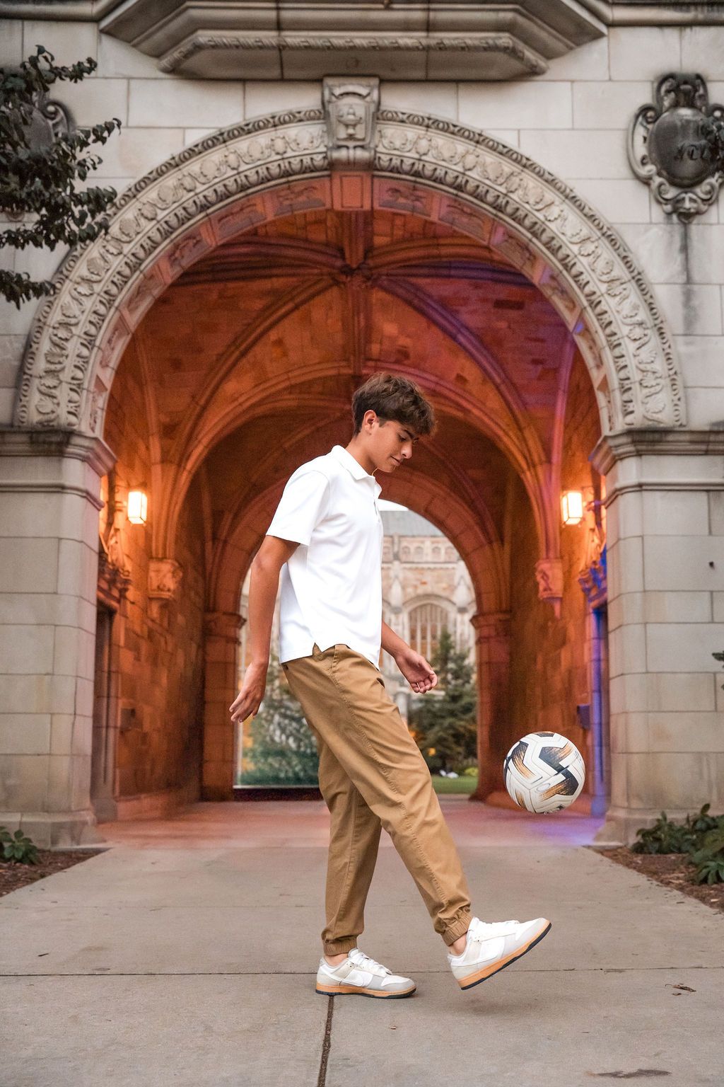 A person performs freestyle soccer tricks under a stone archway illuminated by warm lighting.