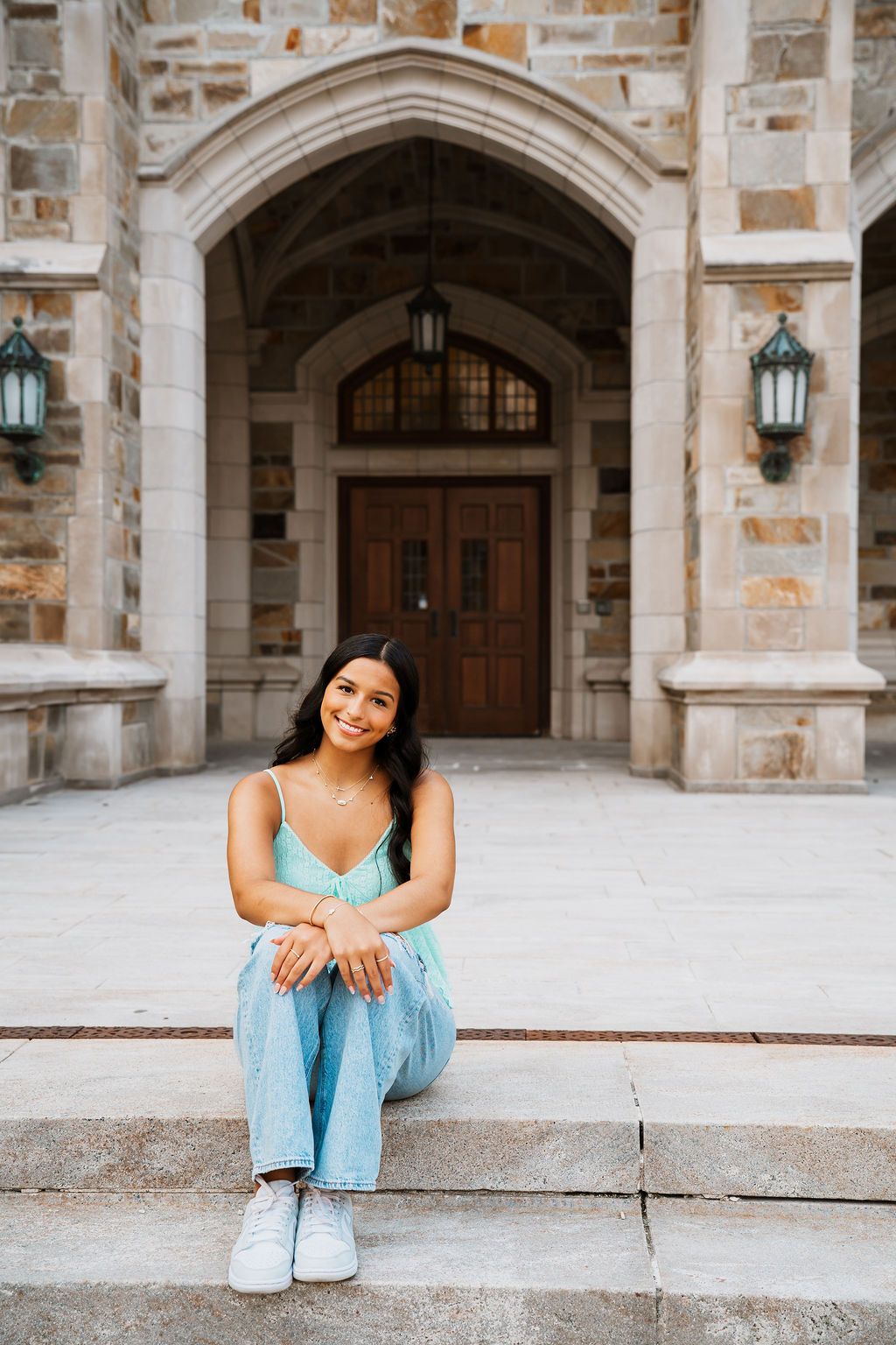 A person in a light blue outfit sits on stone steps in front of a gothic archway entrance with lanterns.