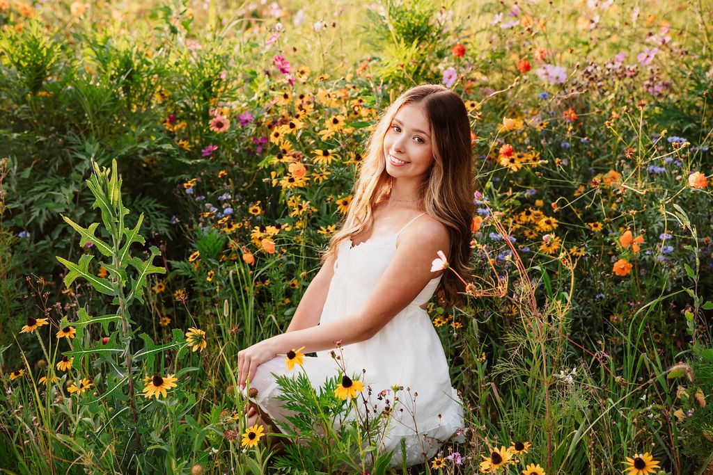 A white sundress stands out against a vibrant wildflower meadow filled with orange and pink blooms at golden hour.