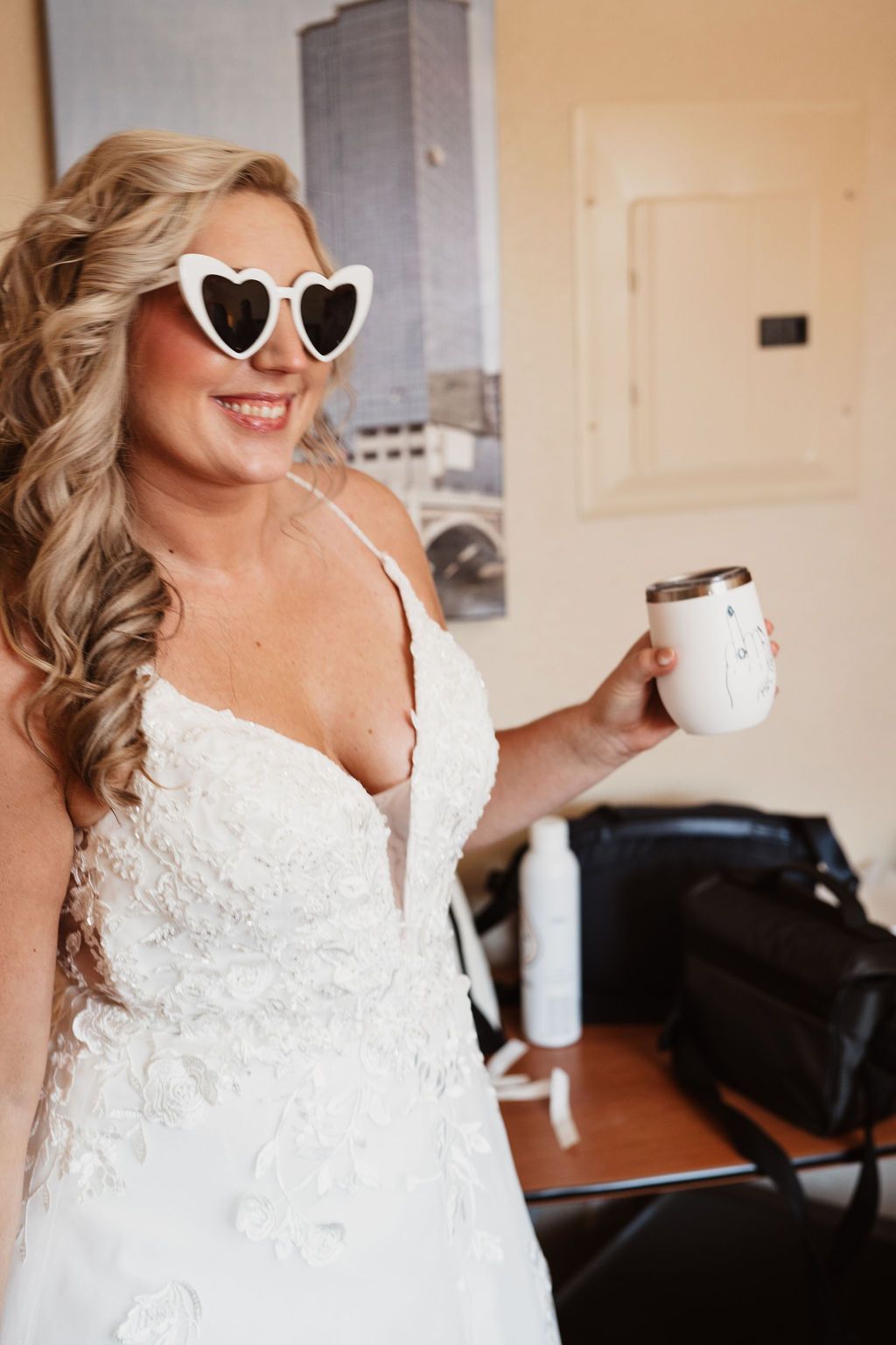 Bride in lace wedding dress gets ready while wearing heart-shaped sunglasses.