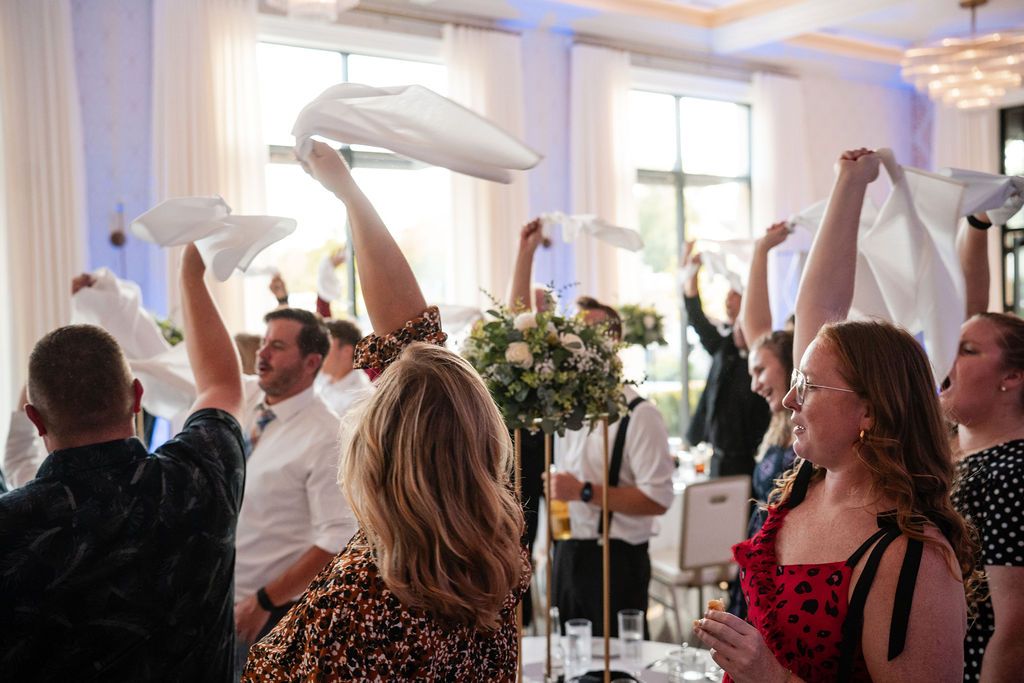 Wedding reception guests raising hands in celebration during indoor event.