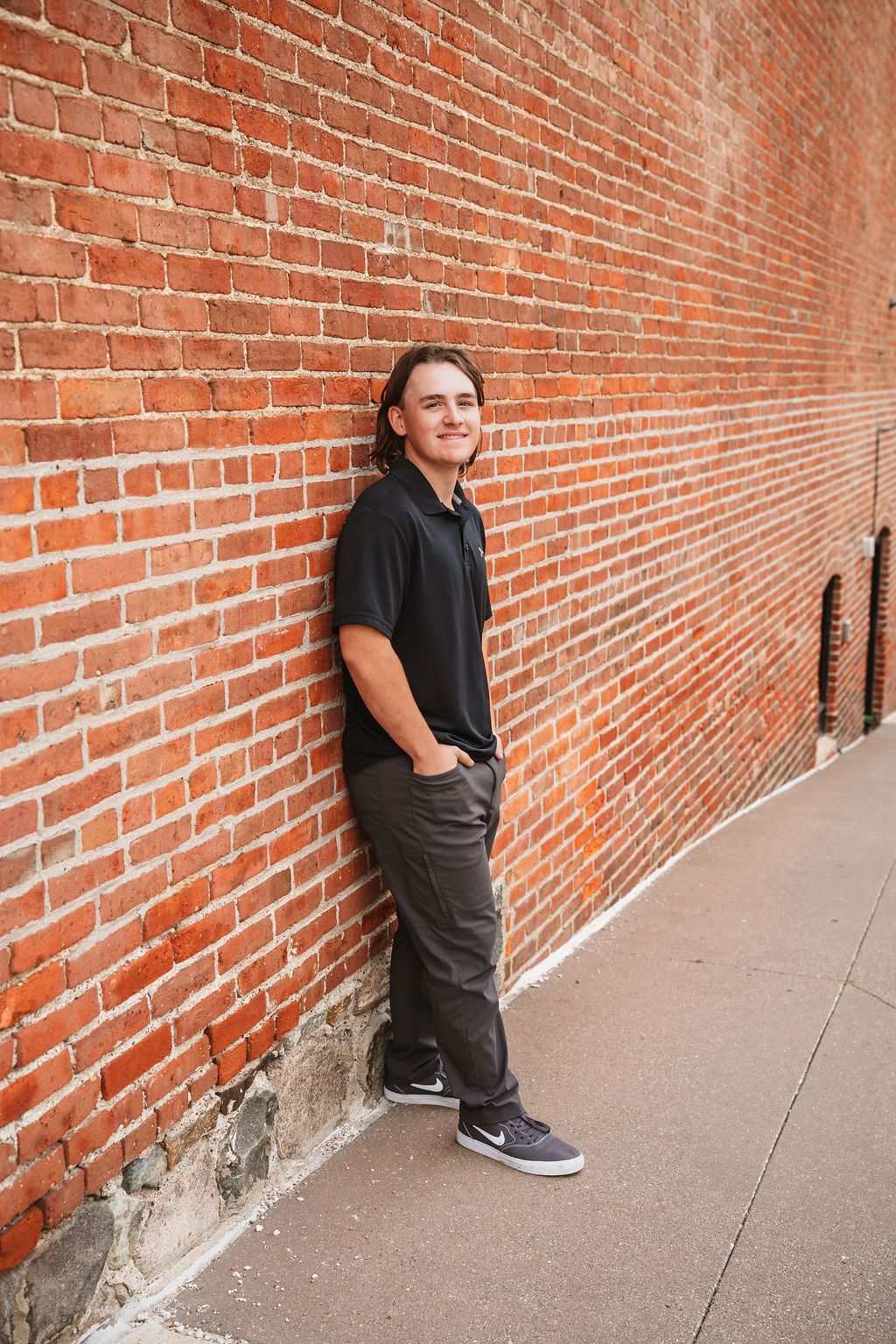 Person in dark clothing leans against red brick wall in urban setting creating dramatic architectural composition.