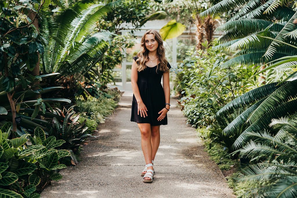 A person in a black dress walks along a lush tropical garden path surrounded by vibrant green palm fronds.