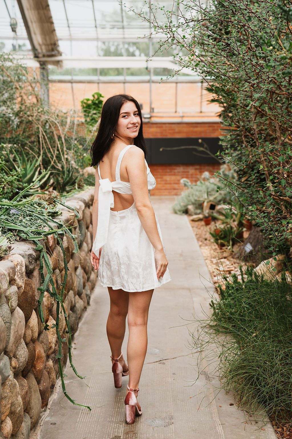 Woman in white dress walks along stone-lined garden path on sunny day.