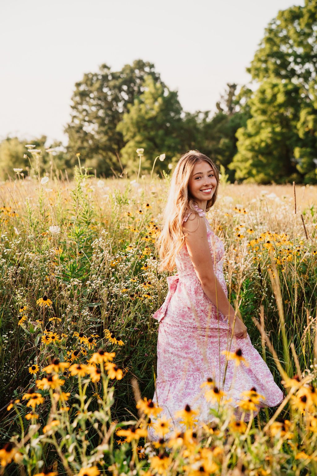 A pink floral dress stands out among yellow wildflowers in a sunny meadow during golden hour.