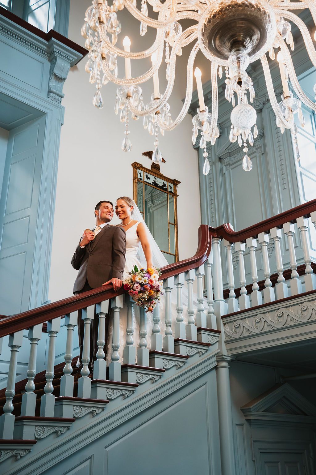 Elegant staircase scene with ornate chandelier and white balustrade in a historic venue.