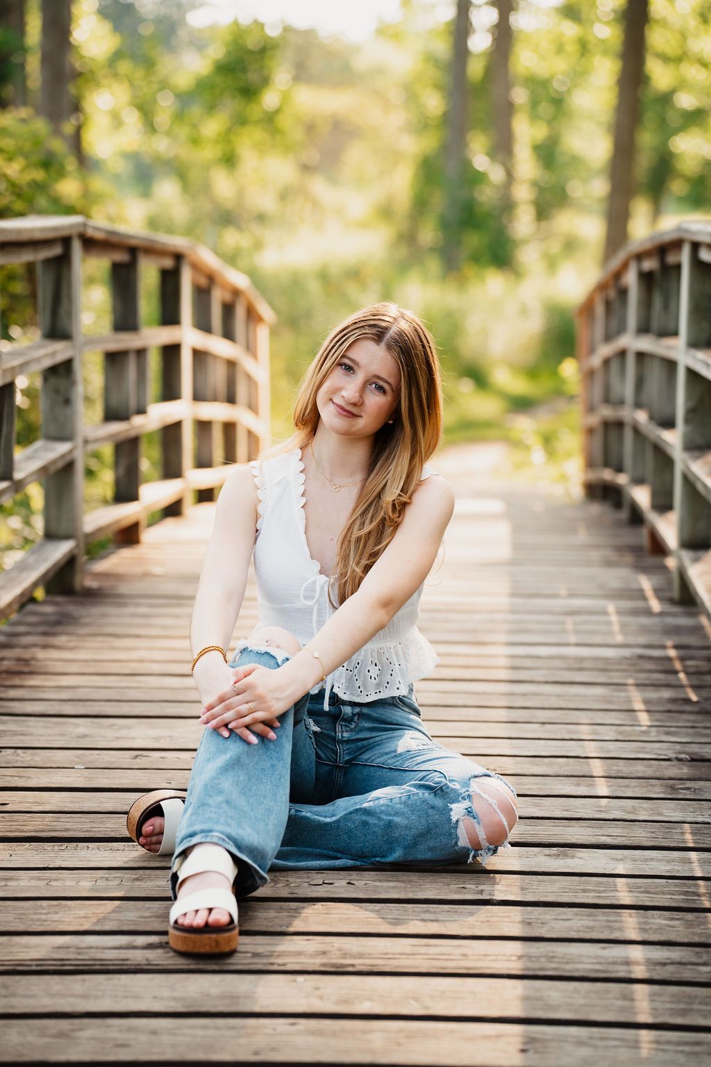 Casual outdoor photoshoot on a wooden bridge walkway surrounded by lush green trees. Matthai botanical gardens senior photos