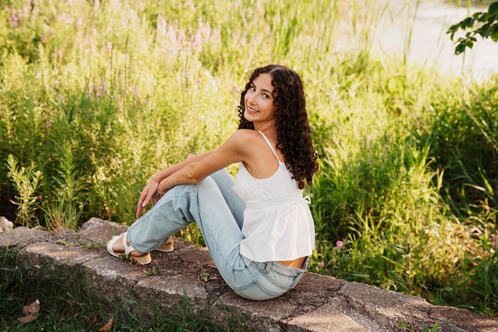 A person in a white top and light jeans relaxes on a grassy hillside during golden hour.