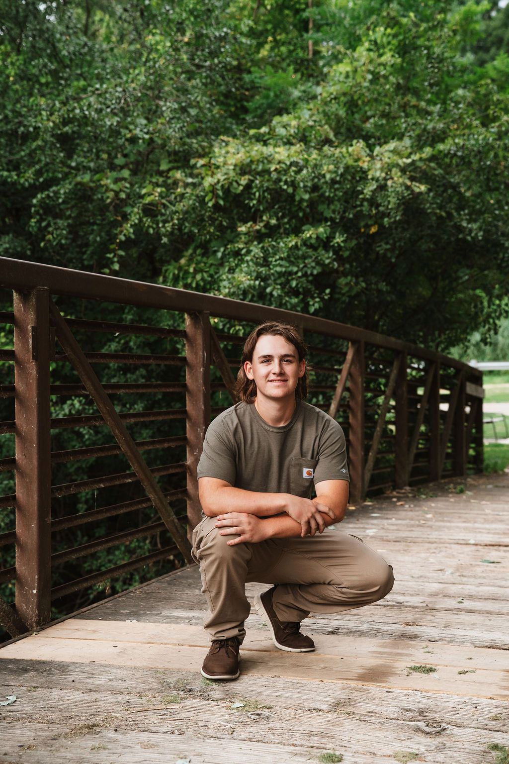 A person in brown clothing sits in various poses on a wooden bridge surrounded by lush green trees.